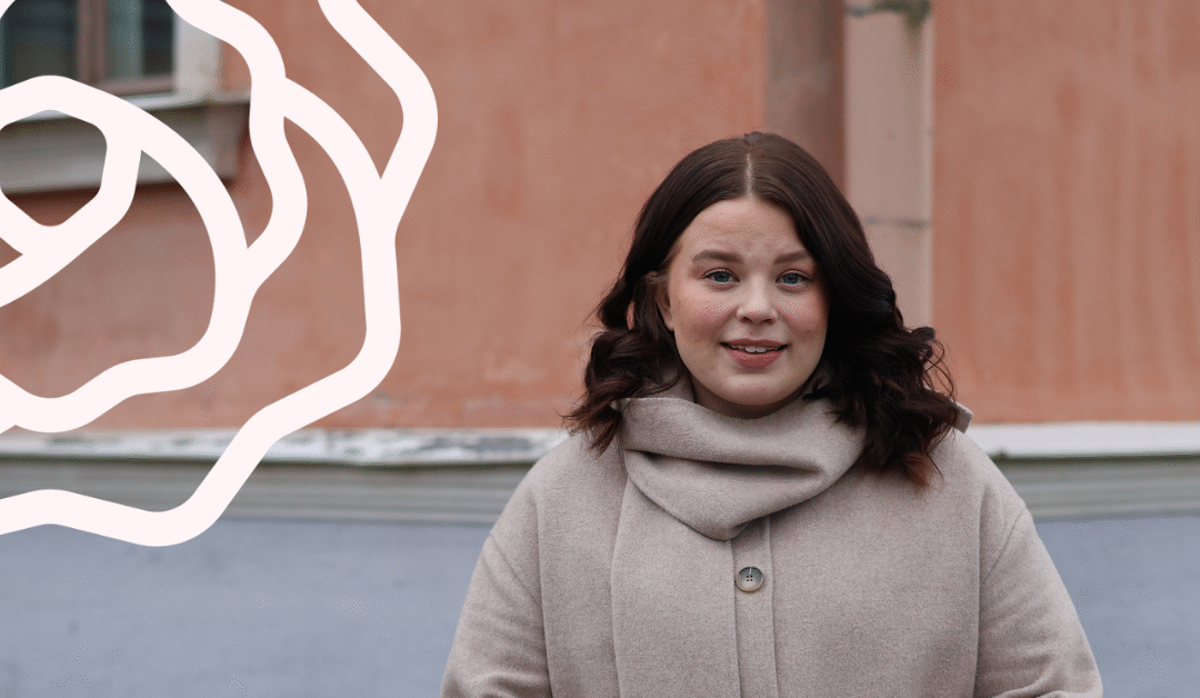 Nainen seisoo oranssin seinän edessä ja hymyilee.