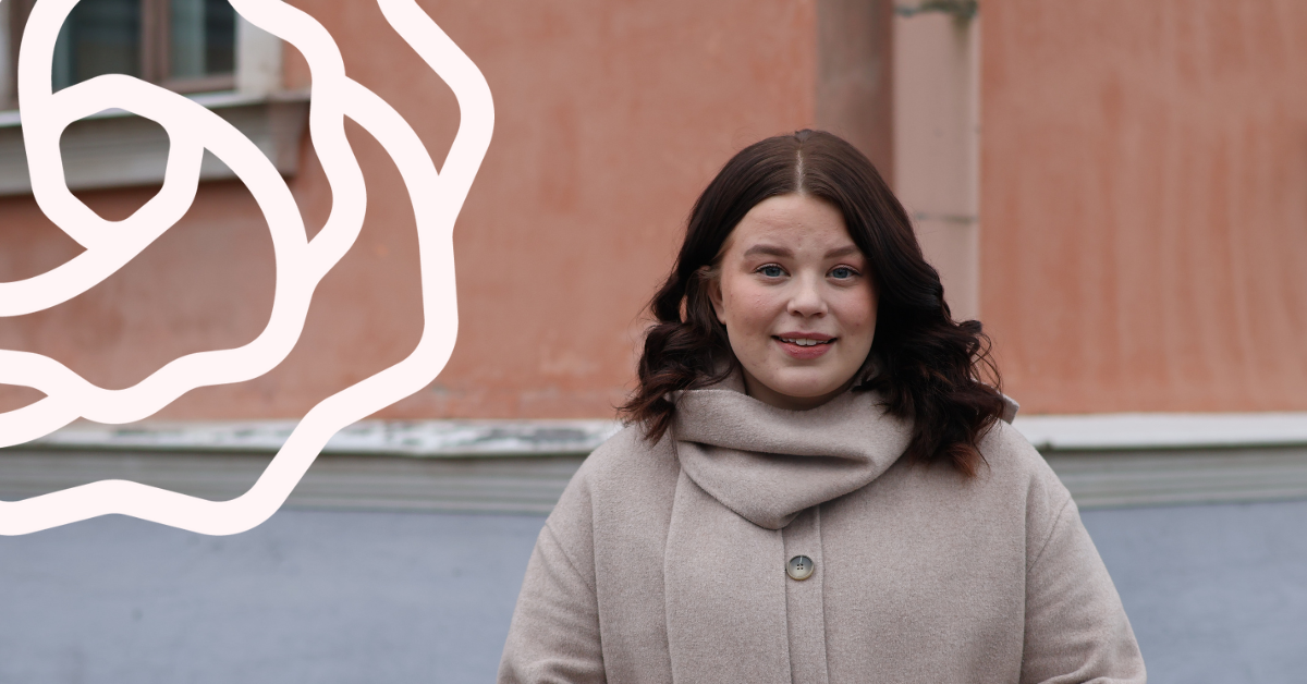 Nainen seisoo oranssin seinän edessä ja hymyilee.