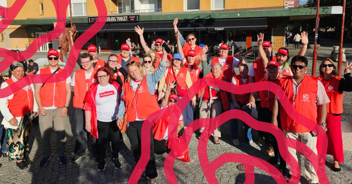 Noin 30 henkilöä katsoo kameraan ja vilkuttaa, osa siristää kirkkaan auringonvalon takia. Monet nauravat tai hymyilevät. Koko porukalla on päällä punaiset Ruotsin sosialidemokraattien liivit.